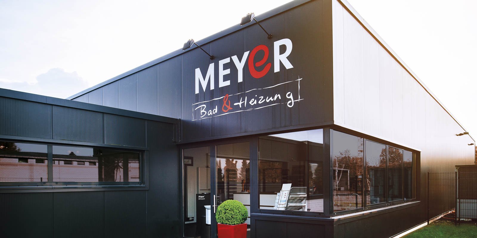Das moderne Gebäude mit der Aufschrift 'MEYER Bad & Heizung' hat große Fenster und eine stilvolle Fassade.