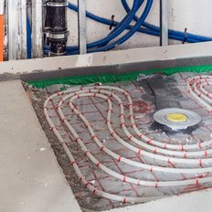 In einem Bauprojekt sind Heizungsrohre sichtbar, die auf einer Folie angeordnet sind, um eine effiziente Fußbodenheizung zu ermöglichen.