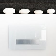 Eine moderne, weiße Betätigungsplatte mit zwei silbernen Tasten, unter einem schwarzen Fliesenhintergrund und weißen Steinen.