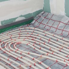 Die Installation einer Fußbodenheizung zeigt geschwungene Rohre, die auf einer isolierenden Folie in einem renovierten Raum liegen.